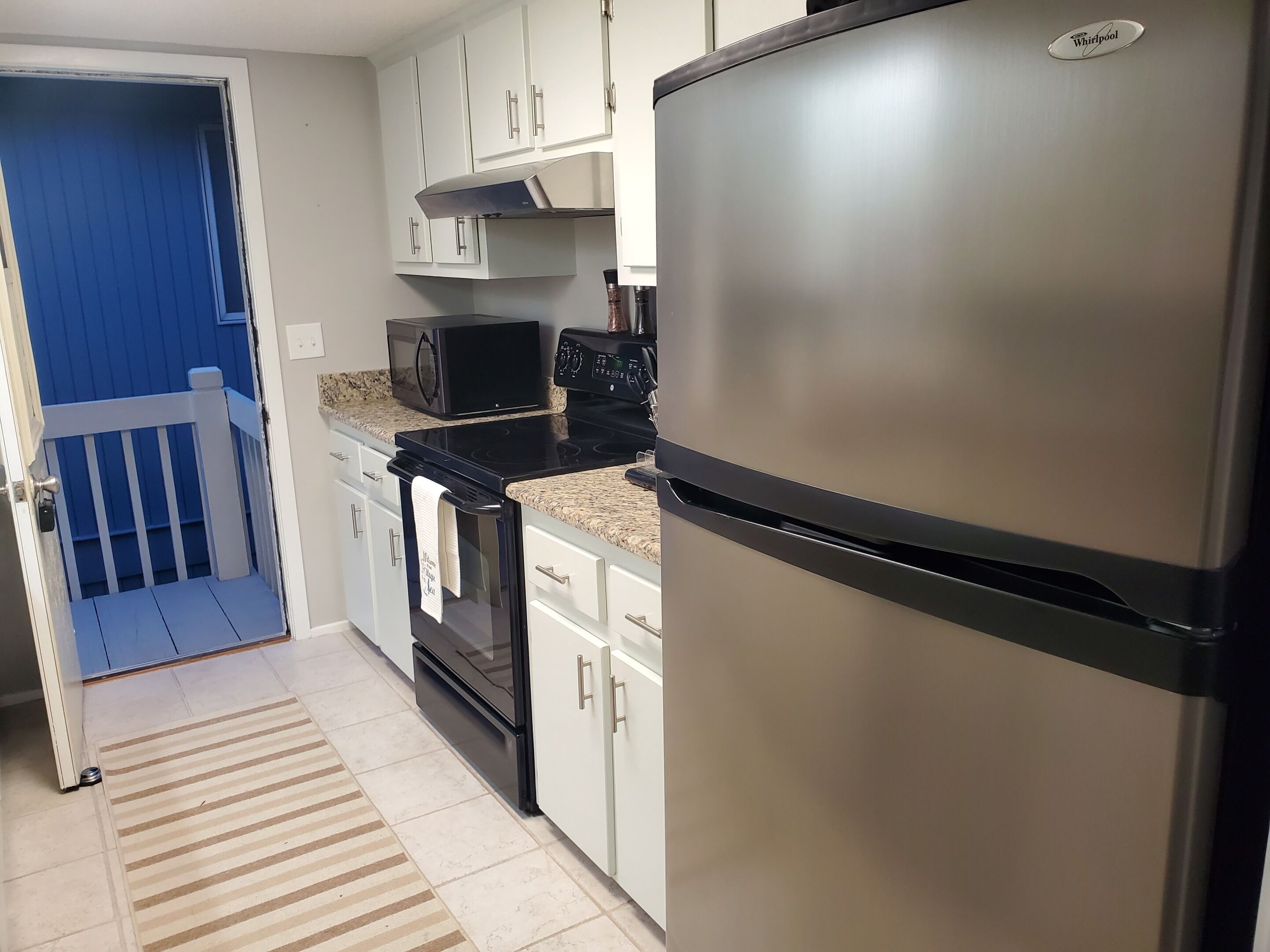 A kitchen with white cabinets, a stainless steel refrigerator, a microwave, and a stove.