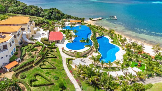An aerial view of a resort with a large swimming pool, beachfront, and lush landscaping.