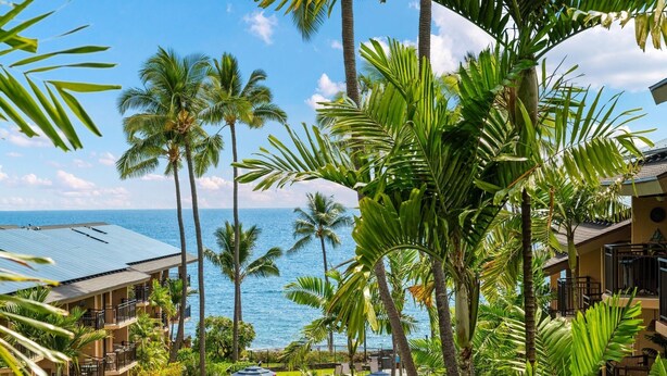 A resort with multiple-story buildings, a pool, and palm trees overlooking the ocean.