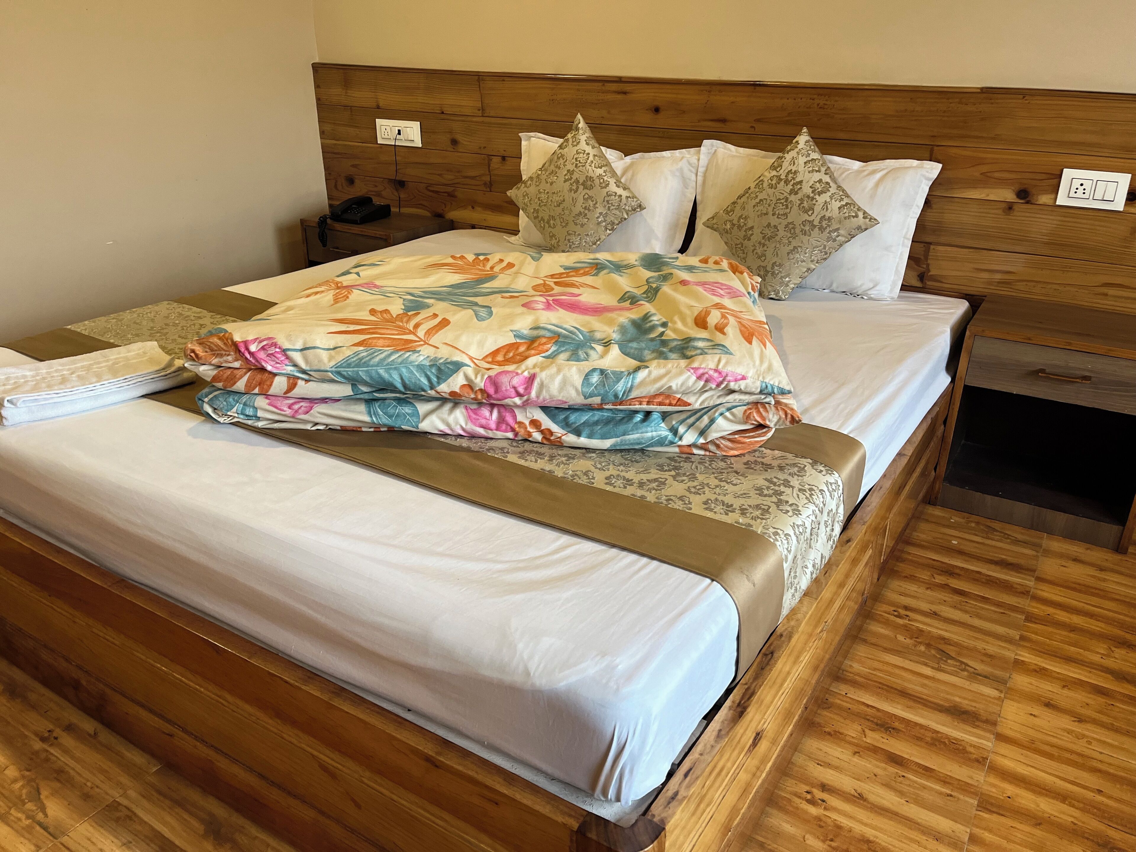 Uma cama bem arrumada com colcha florida e almofadas decorativas, uma cabeceira de madeira e uma mesa de cabeceira com um telefone e um abajur.