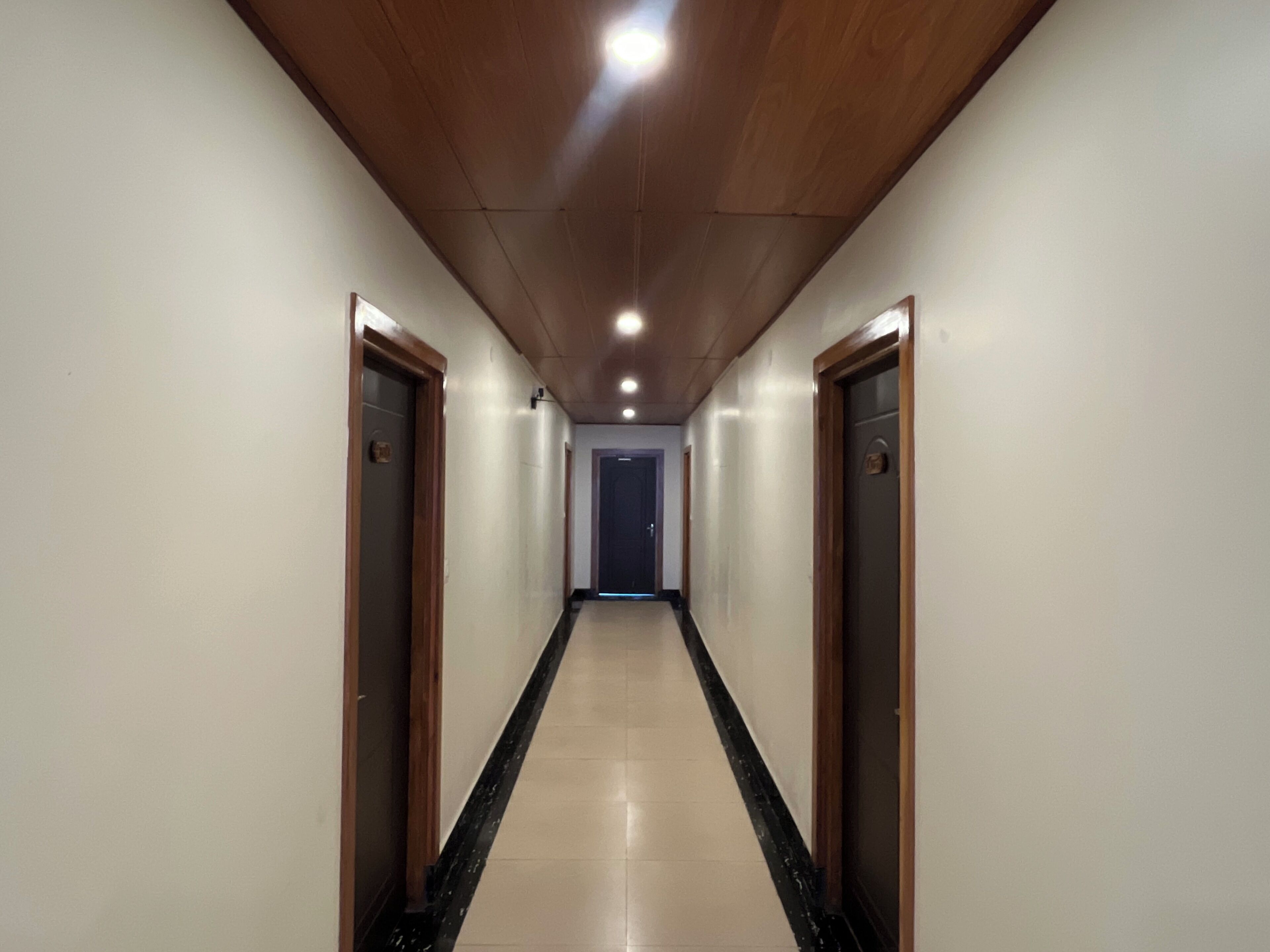 Un long couloir étroit, avec des portes en bois de chaque côté et un sol carrelé.