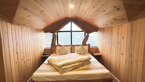 Une pièce chaleureuse, aménagée dans une cabane en bois, avec un plafond en pente, un grand lit avec des oreillers, une table de chevet et une fenêtre offrant une belle vue.