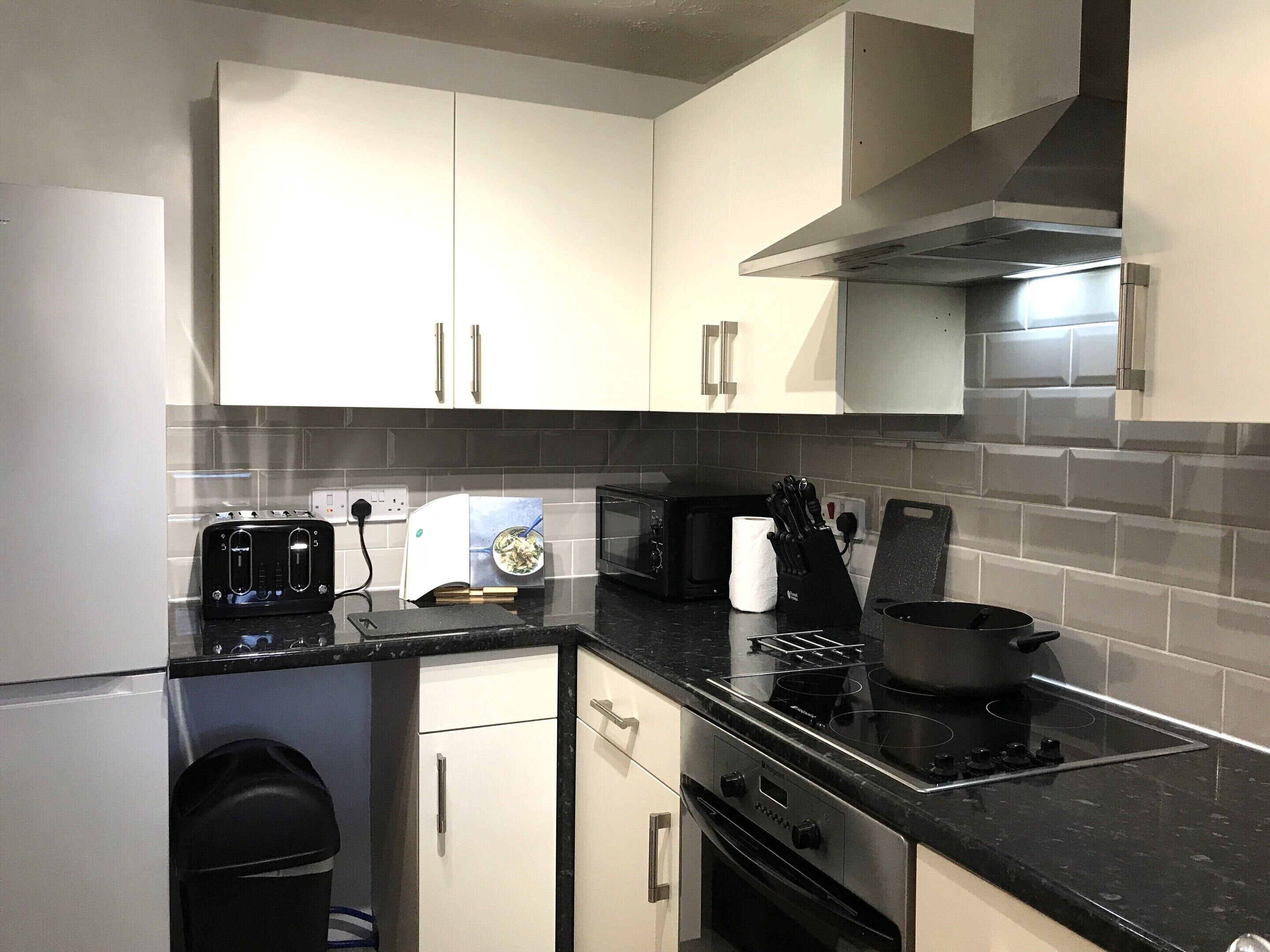 A modern kitchen with white cabinets, a black countertop, a microwave, a toaster, and a stove.