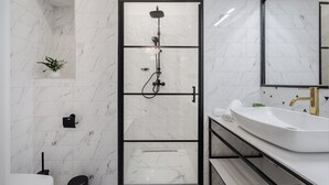 A modern bathroom with a glass-enclosed shower, a white sink, and a marble-tiled wall. - Astoria Boutique Suites - by BQA (Budapest)