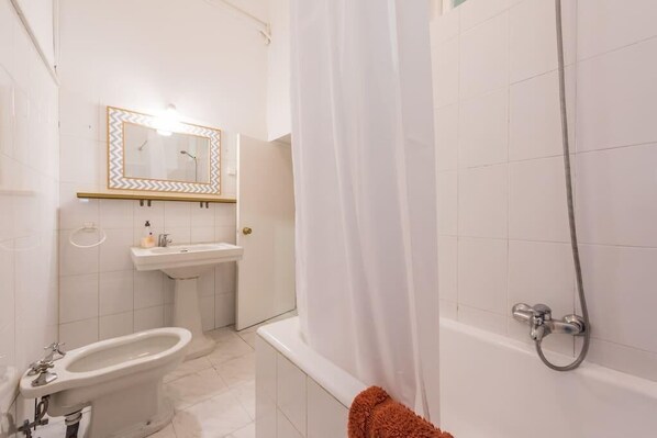 A bathroom with a bathtub, a sink, a bidet, and a mirror with a zigzag frame.