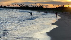 A beach with people surfing and walking along the shore. - Summer Ville Itacimirim (Camaçari)