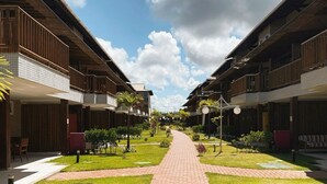 A pathway leading to a row of modern buildings with balconies, surrounded by well-maintained grass and small plants. - Summer Ville Itacimirim (Camaçari)