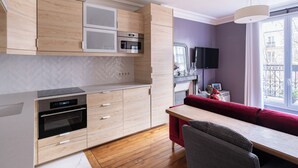 Una cucina moderna con elettrodomestici integrati, un'area pranzo con divano rosso e vista sulla città attraverso ampie finestre.