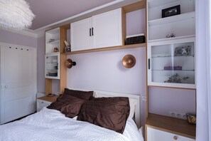 A bedroom with a bed, white wardrobe, and built-in shelves with various items.