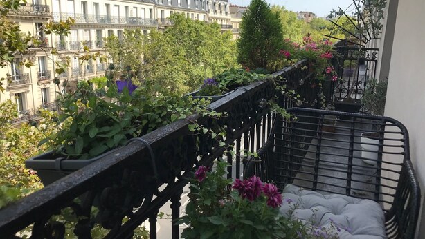 Un balcone con vista sugli edifici parigini, piante in vaso e una zona salotto con cuscineria.