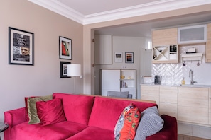 A living room with a red sofa, a kitchen area with wooden cabinets, and a white countertop.