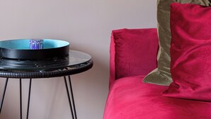 Una stanza con un quadro appeso al muro, un tavolo rotondo in vetro con base nera e un divano rosso con un cuscino verde.