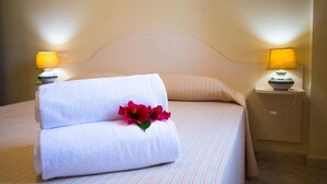 A neatly made bed with two white towels and a decorative flower, a bedside lamp, and a nightstand with a bowl. - Relaxing Le Residenze del Maria Rosaria No2222 (Orosei)