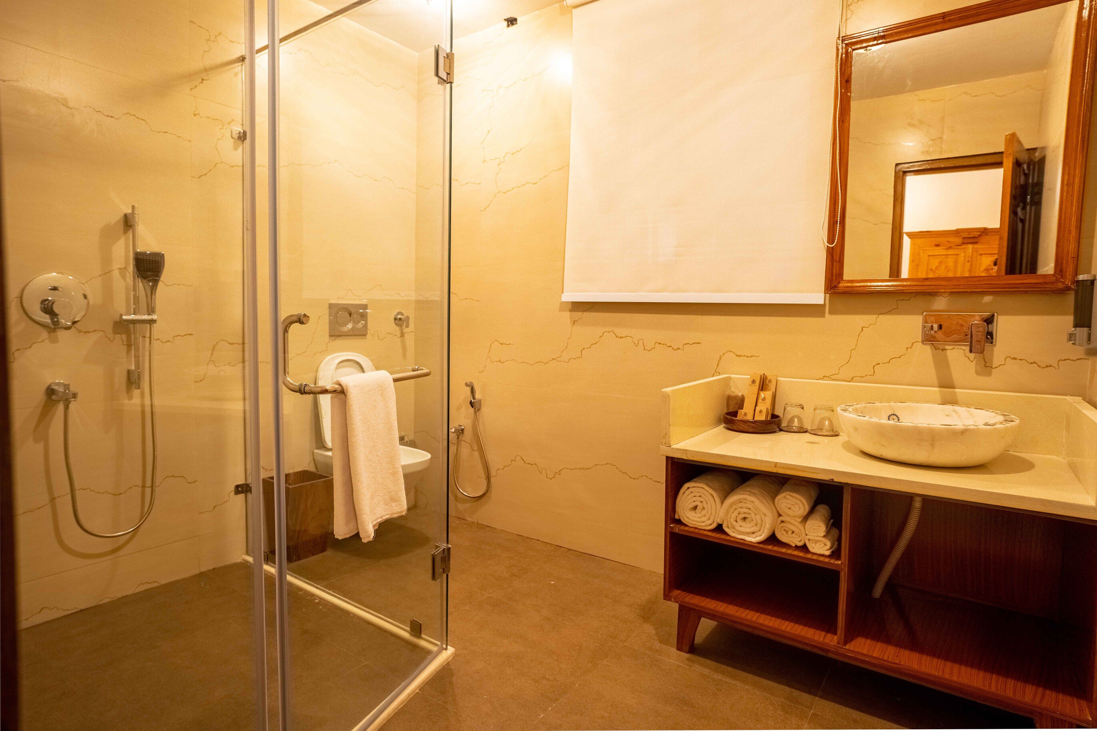 Un baño con ducha de vidrio, lavamanos con encimera de mármol y tocador de madera con repisas para toallas.