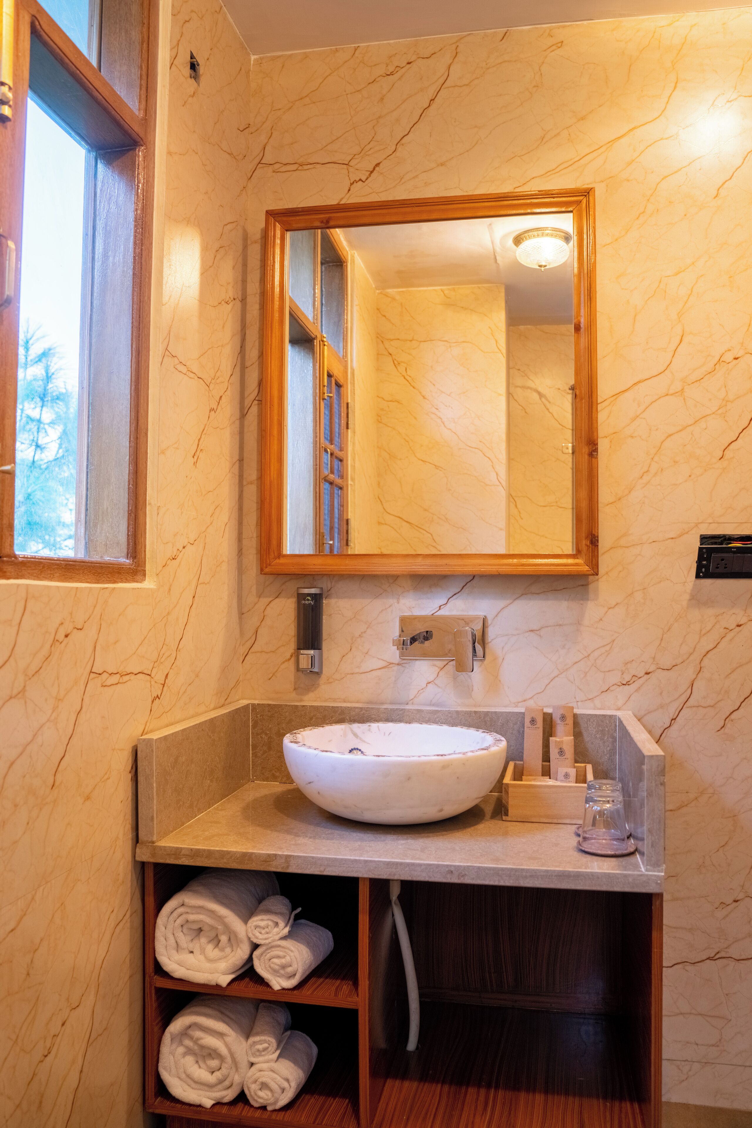 Un bagno con una parete in marmo, uno specchio con cornice in legno, un lavandino bianco e un portasciugamani con asciugamani.