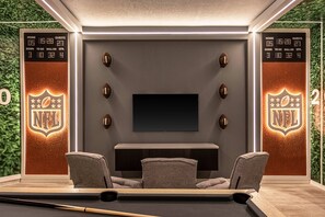 Un cine en casa con un televisor de pantalla plana, dos sillones reclinables, una mesa de billar y decoración temática de la NFL.