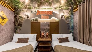Una habitación temática con dos camas, un banco de madera y un cartel de 'Jurassic Park'.