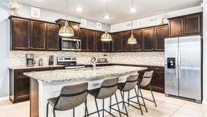 A modern kitchen with dark wood cabinets, stainless steel appliances, a large island with bar stools, and pendant lighting.