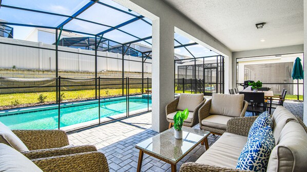 A spacious outdoor area with a swimming pool, wicker furniture, and a glass-enclosed patio.