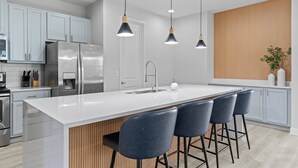 Een moderne keuken met een groot schiereiland, barstoelen, roestvrijstalen apparatuur en hanglampen.