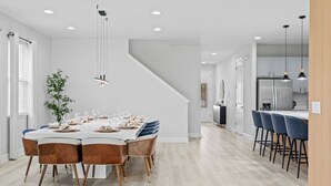 Een moderne eetruimte met een witte tafel voor zes personen, houten stoelen en hanglampen.