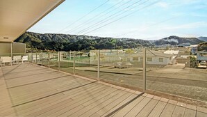 Un balcon donnant sur un paysage vallonné, un espace de stationnement et un bâtiment doté d’un toit plat.