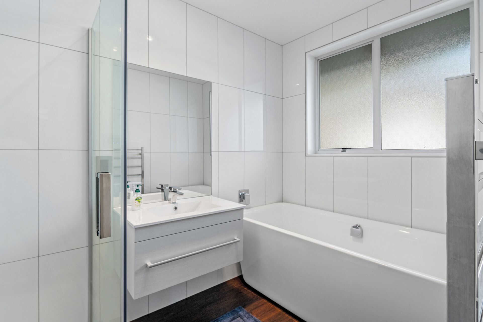 Ein modernes Badezimmer mit weißen Fliesen, einer Glasdusche, einem Doppelwaschtisch und einer freistehenden Badewanne.
