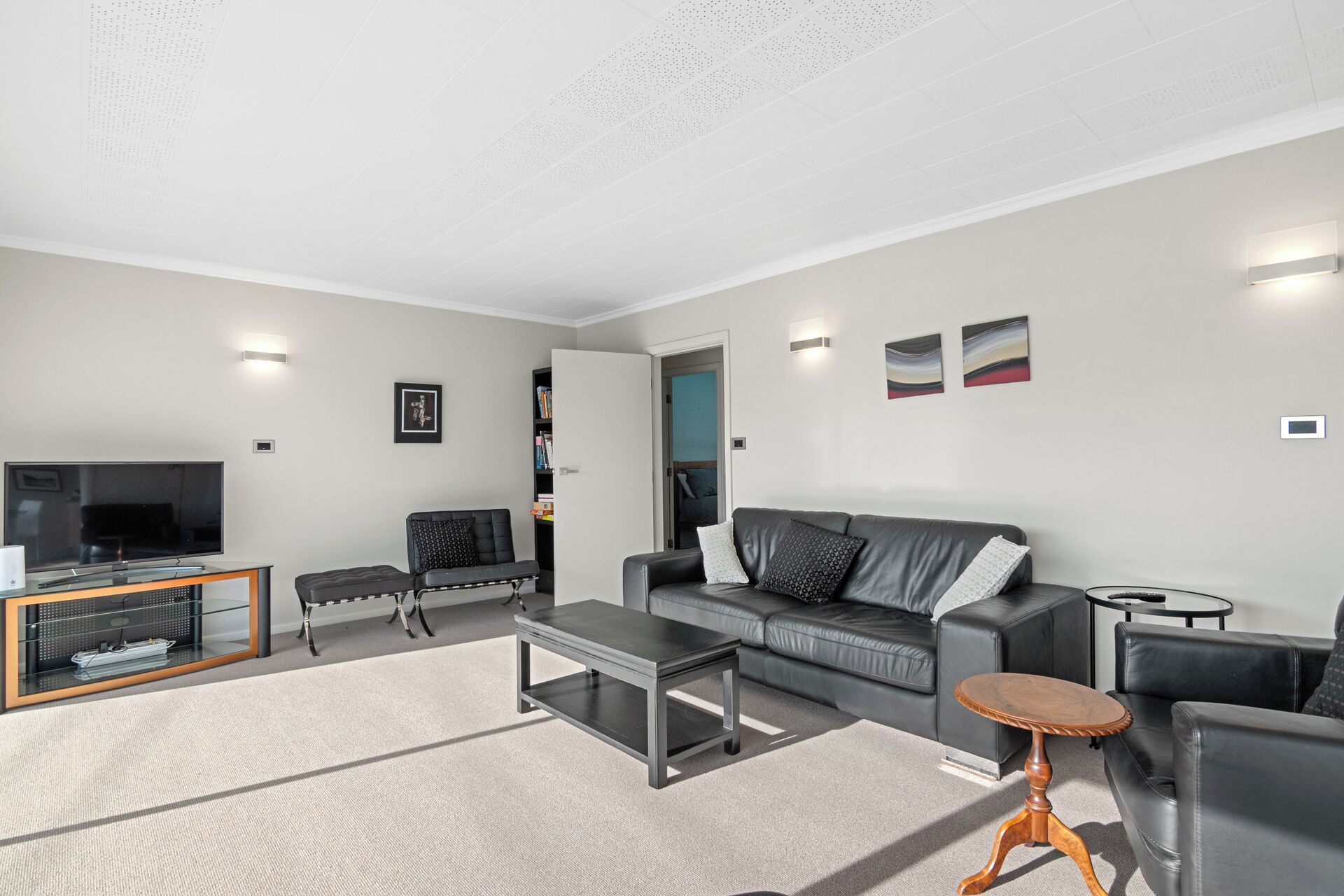 Een moderne woonkamer met een flatscreen televisie, leren banken, een salontafel en een boekenplank.