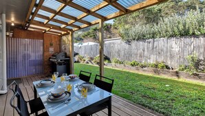 Une terrasse extérieure avec une table dressée pour le repas, un barbecue et une clôture en bois en arrière-plan.
