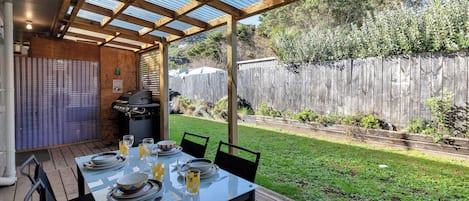 Een terras buiten met een eettafel, een barbecue en een houten hek op de achtergrond.