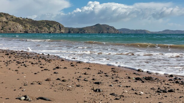 Une plage au paysage rocheux et aux vagues calmes.