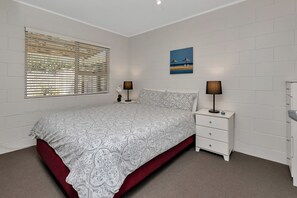 A bedroom with a bed, two bedside tables, a nightstand, a wall-mounted lamp, and a painting.