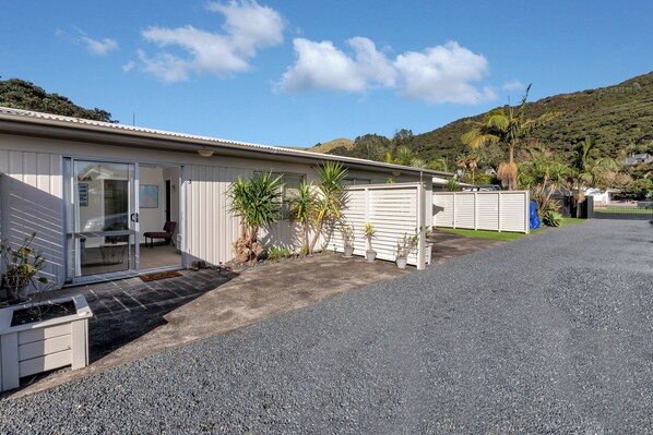 A single-story building with a covered patio, potted plants, and a gravel driveway.