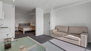 A modern hotel room with a bed, a sofa, a coffee table, and a kitchenette area.