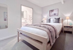 Un dormitorio moderno con cama, mesitas de noche, un espejo y un cuadro en la pared.