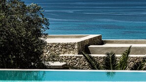 Ein Pool mit klarem, blauem Wasser, einer Steinmauer und Blick auf den Ozean.