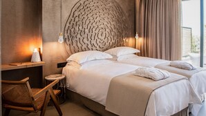 Ein modernes Hotelzimmer mit einem großen Bett, einem Schreibtisch, einem Sessel und Blick ins Freie.
