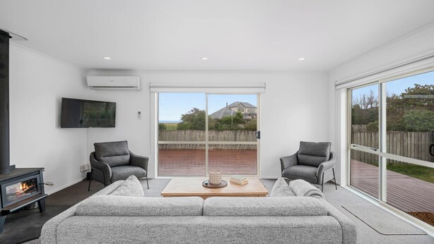 A modern living room with a fireplace, grey sofas, and a large sliding glass door leading to a deck. - Lakeside Haven - Taupo Holiday Home (Wharewaka)