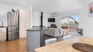 A modern kitchen with a built-in fridge, a dining area with a wooden table, and a seating area with a grey sofa. - Lakeside Haven - Taupo Holiday Home (Wharewaka)