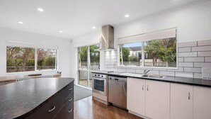 A modern kitchen with white cabinets, stainless steel appliances, and large windows offering views of the outdoors. - Lakeside Haven - Taupo Holiday Home (Wharewaka)