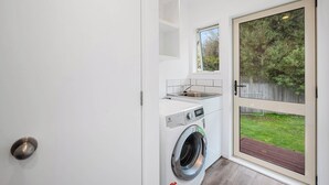 A compact laundry room with a washing machine, a sink, and a window. - Lakeside Haven - Taupo Holiday Home (Wharewaka)