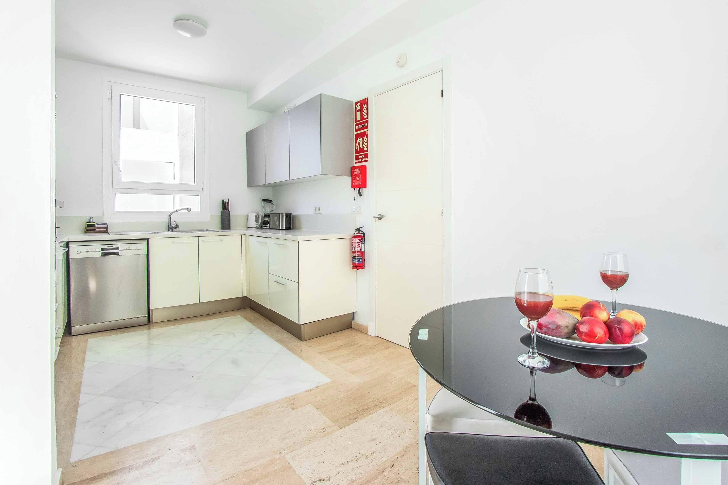 A modern kitchen with a dishwasher, microwave, and a fruit plate on a glass table.