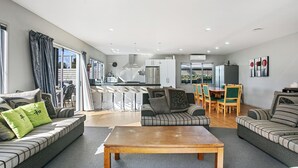 A modern living room with a sofa, a wooden coffee table, and a dining area with a table and chairs. - Family Harmony - Waihi Beach Holiday Home (Waihi Beach)
