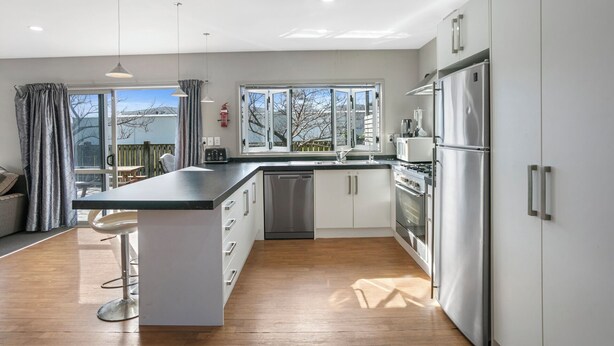 A modern kitchen with a central island, stainless steel appliances, and a large window offering a view. - Family Harmony - Waihi Beach Holiday Home (Waihi Beach)