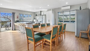 A modern kitchen with white cabinets, a stainless steel refrigerator, and a dining area with wooden chairs and a table. - Family Harmony - Waihi Beach Holiday Home (Waihi Beach)