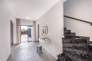 Un interno moderno con una scala, una porta vetrata che dà sull'esterno e un tavolino consolle bianco con uno specchio.