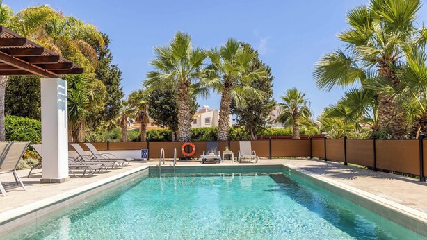 A swimming pool with clear water, surrounded by palm trees and lounge chairs.