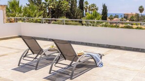 A rooftop terrace with two sun loungers, a hat, and a striped towel.