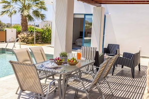 Mesa de vidrio con sillas de metal, una piscina y vista a un dormitorio con cama y ventana.