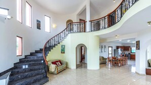 Amplia sala de estar con una escalera curva, una mesa de comedor y una cocina al fondo.